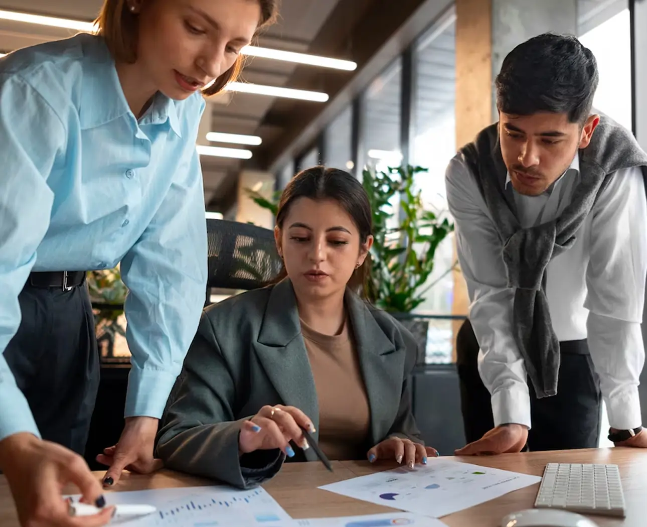 Three professionals discussing documents with charts and graphs at a desk in a modern office.
