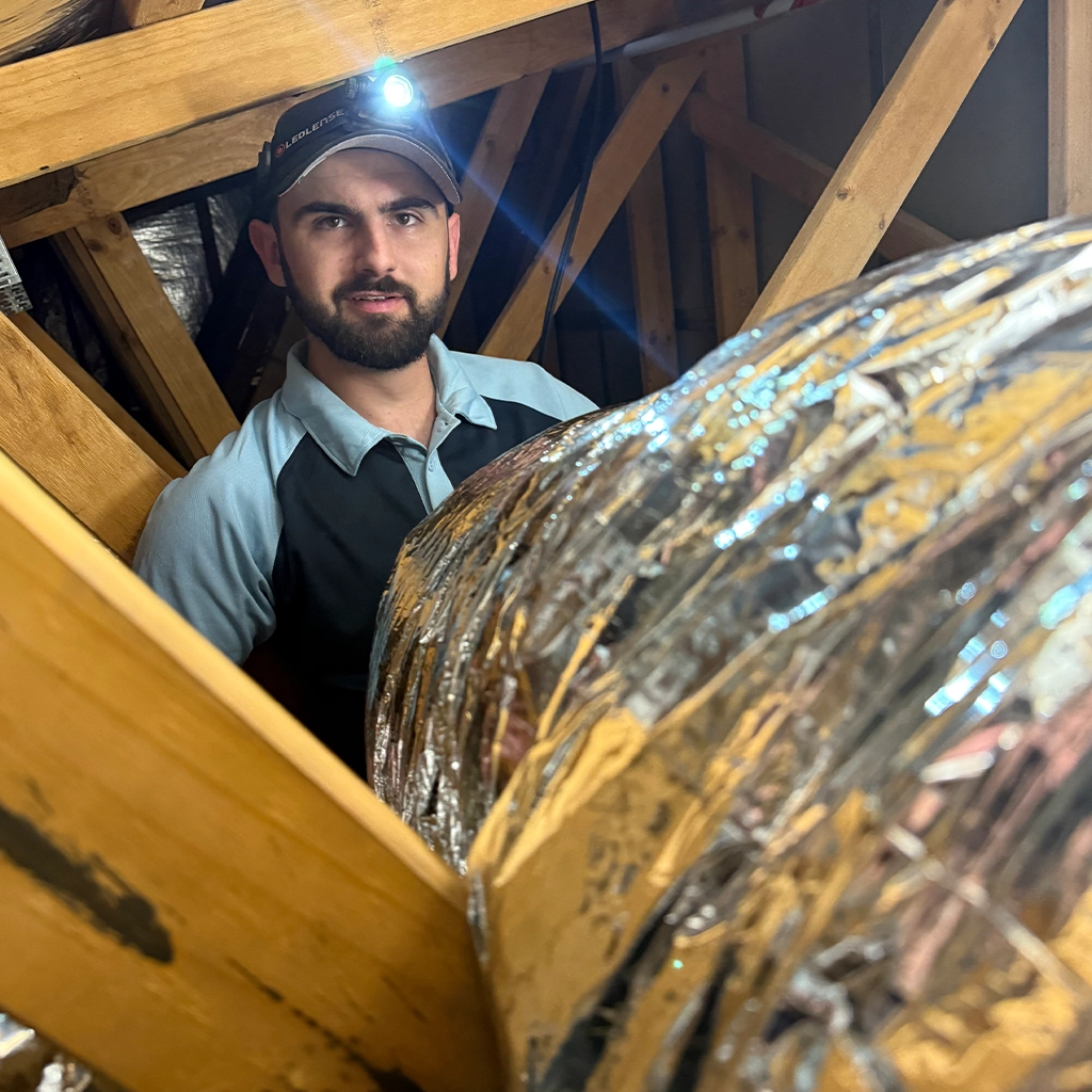 Air conditioning technician inspecting system components in a roof space.