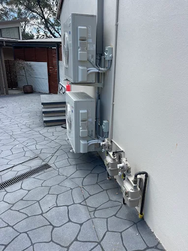 Two Mitsubishi outdoor air conditioning units mounted along a residential exterior wall