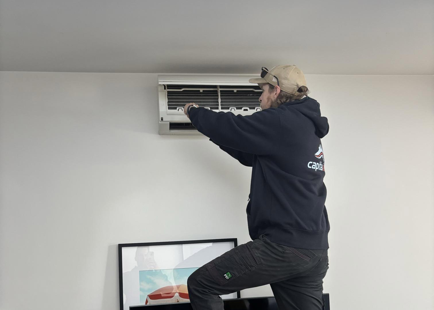 Capital Air technician installing or servicing a wall-mounted split system inside a home.