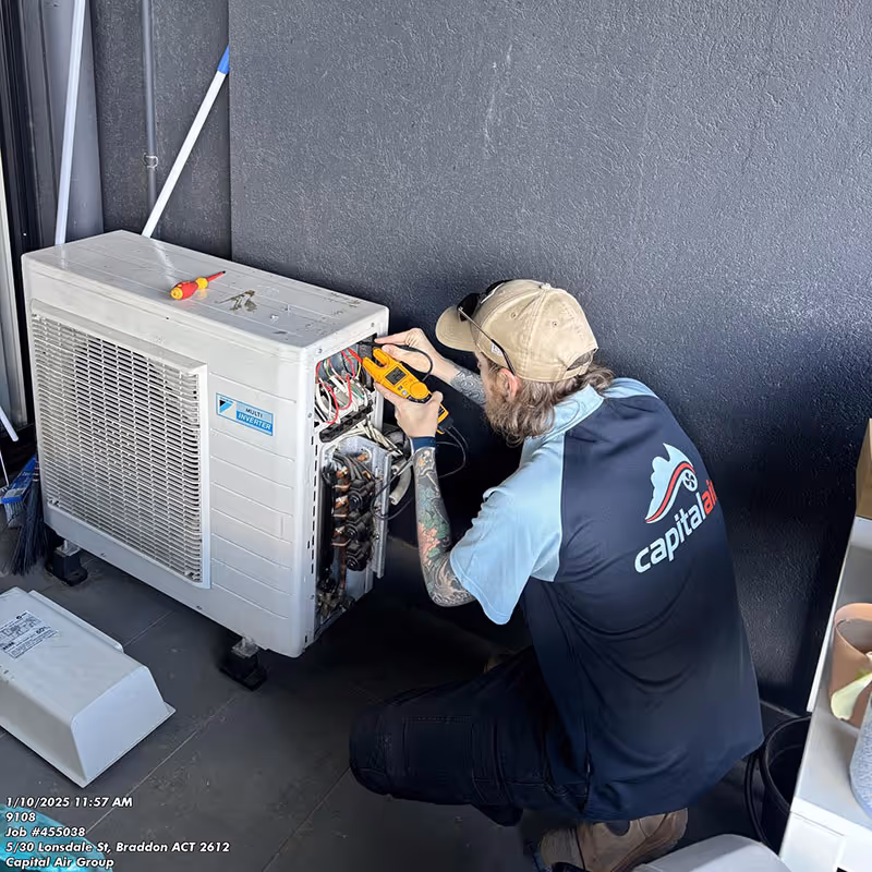 Capital Air technician servicing an outdoor air conditioning unit at a Canberra home.