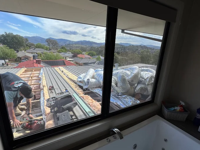 Technician installing ducted air conditioning system on a residential roof in Canberra.