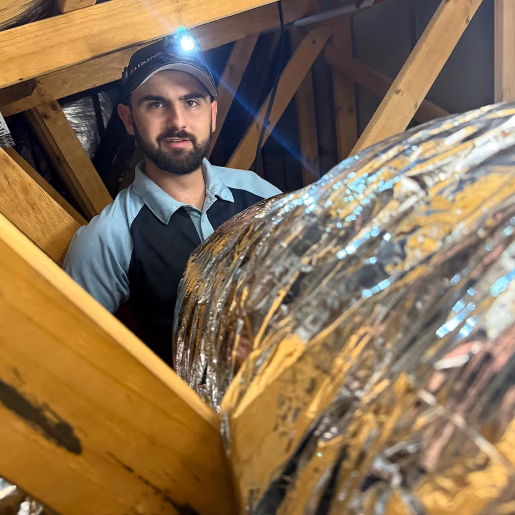 Technician working with ducted air conditioning inside roof structure.