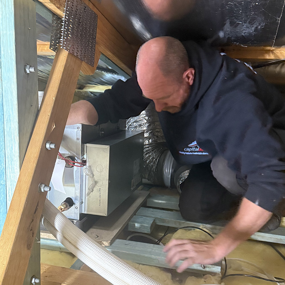 Technician working on ducted heating system inside roof space of Kambah home.