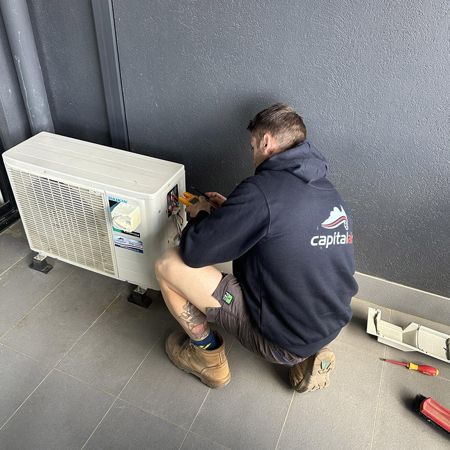 Technician repairing an outdoor air conditioning unit at an apartment property.
