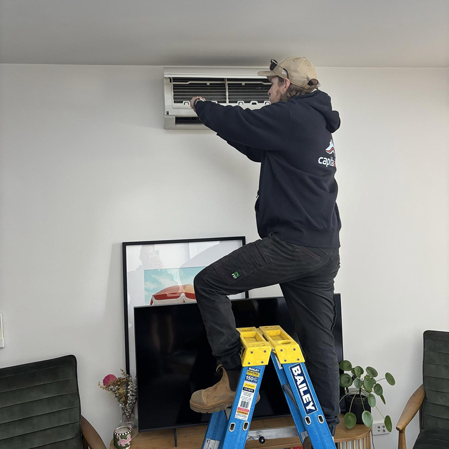 Technician servicing wall-mounted split system inside a modern home.