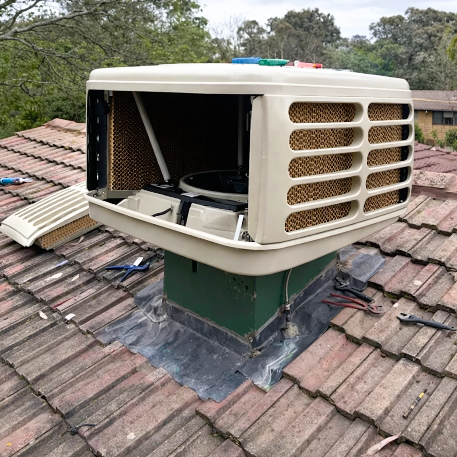 Evaporative cooling unit installed on a tiled roof with tools nearby.