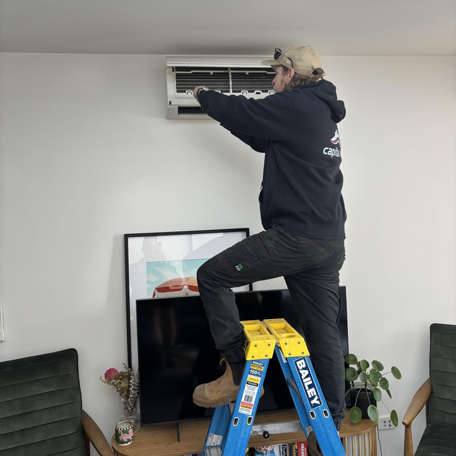 Technician servicing a wall-mounted split system air conditioner inside a home.