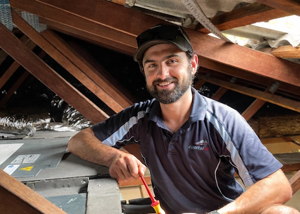 Air conditioning technician inspecting a ducted system inside a ceiling space.