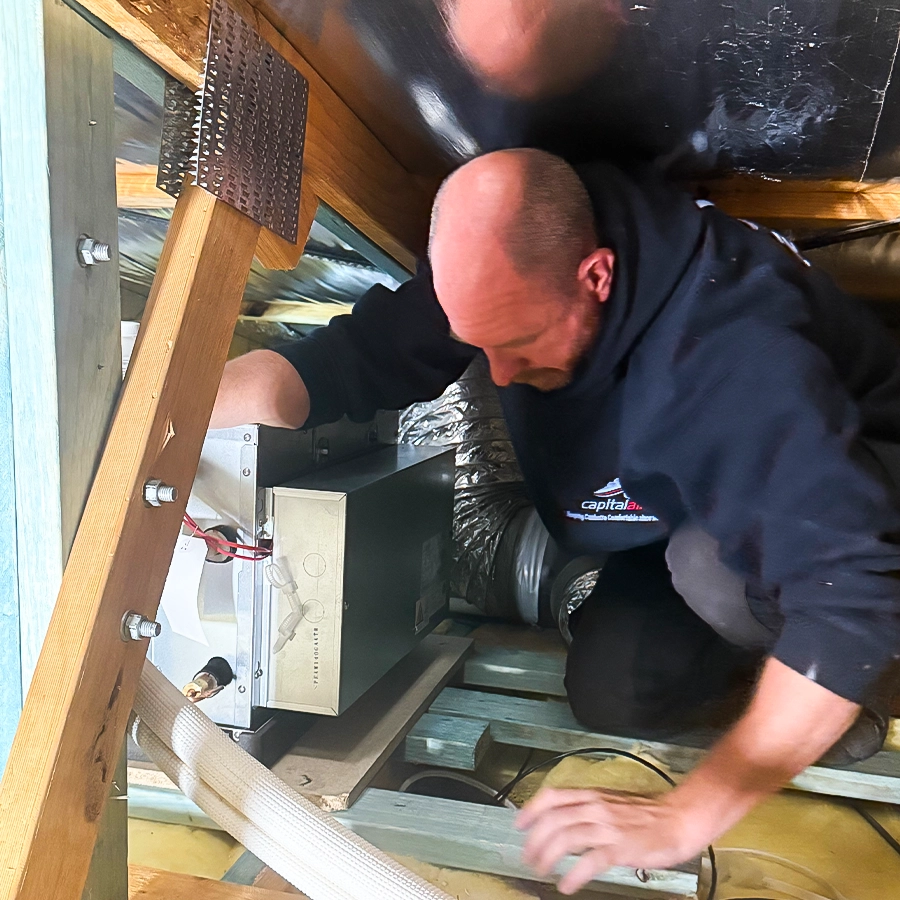 Technician servicing a ducted air conditioning system inside a roof cavity.