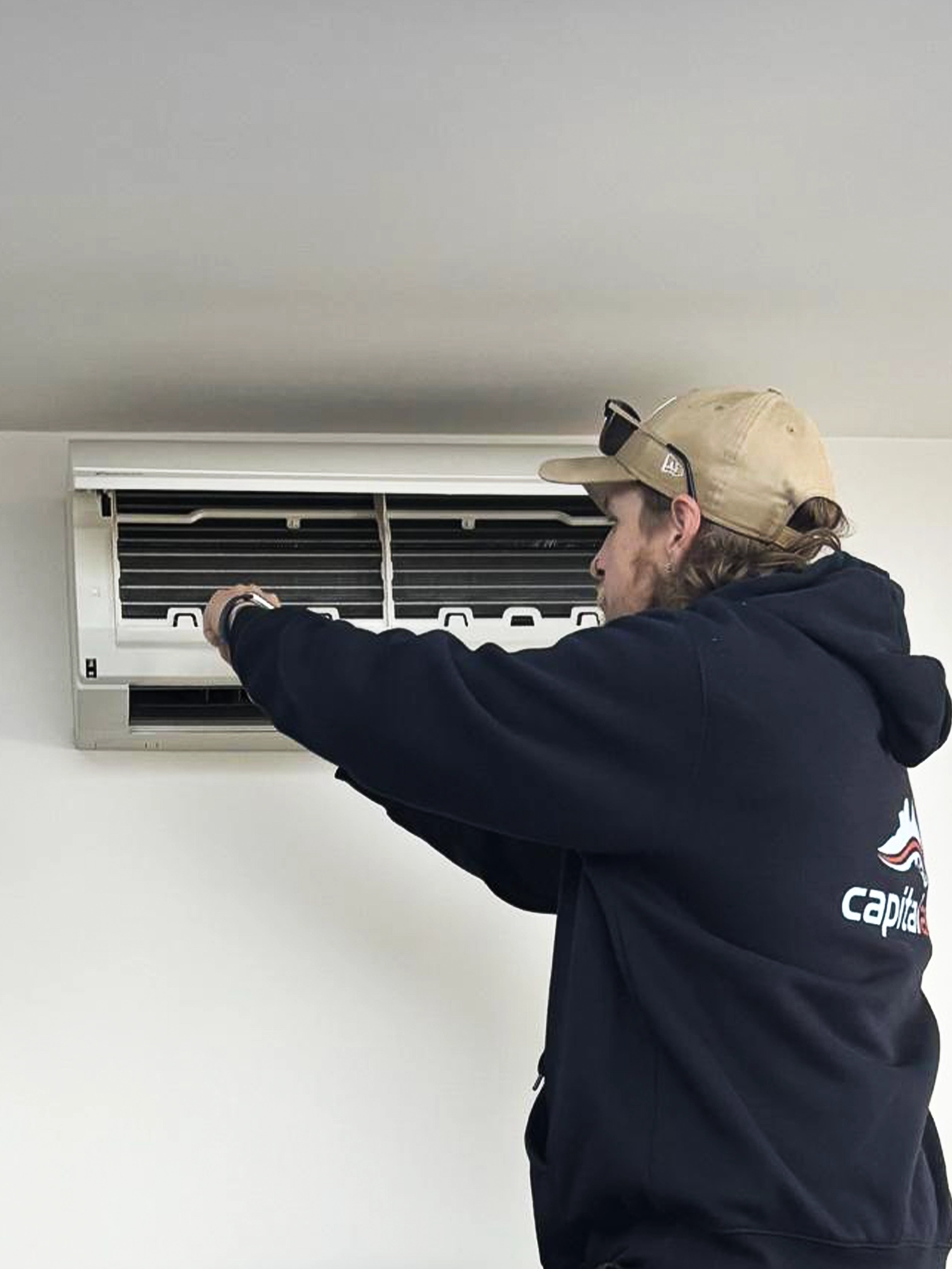 Capital Air technician servicing a wall-mounted air conditioning unit inside a home.