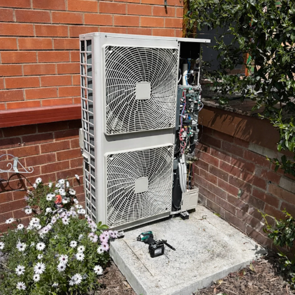 Outdoor air conditioning unit installed beside a brick home with components exposed for repair.