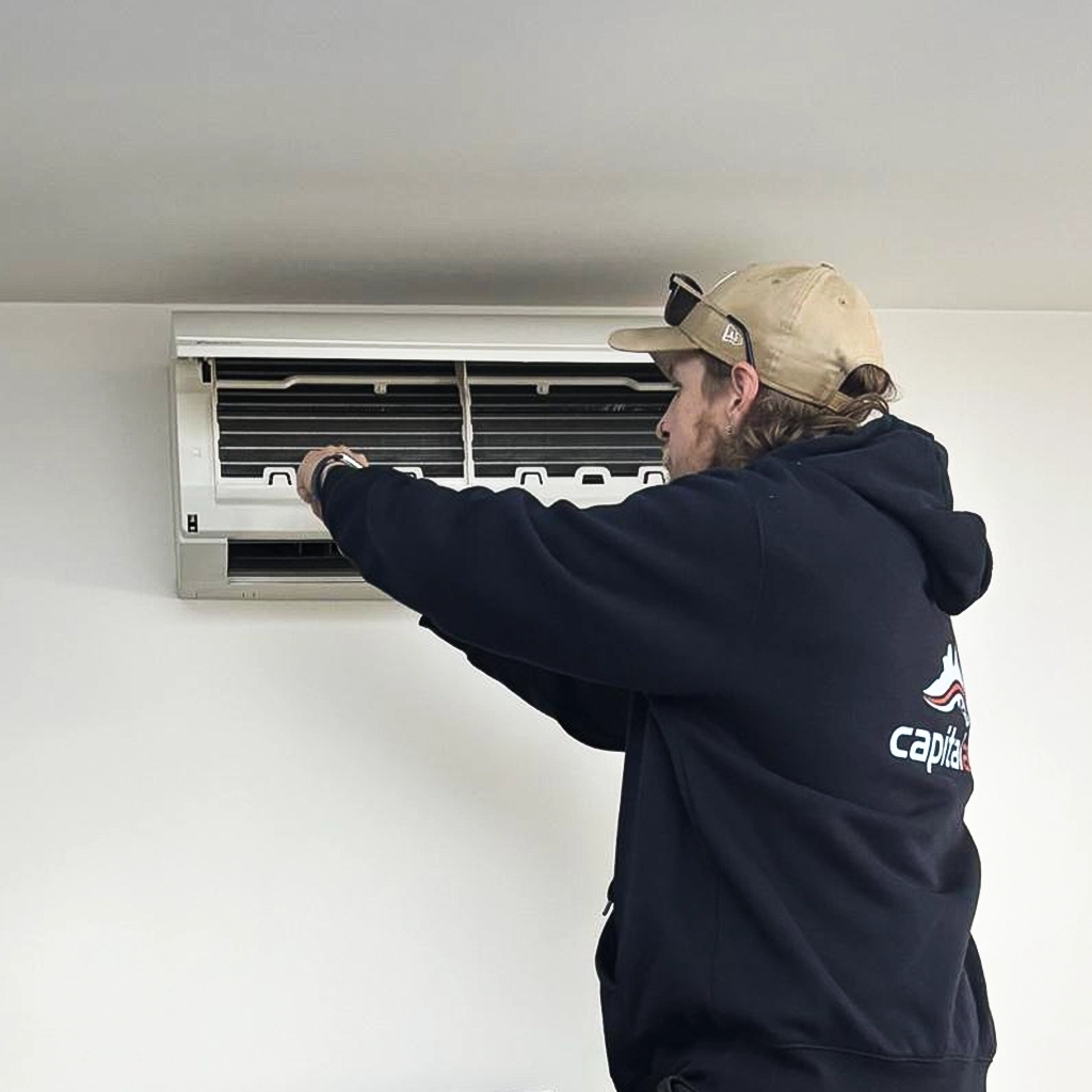Technician cleaning and servicing split system air conditioner.