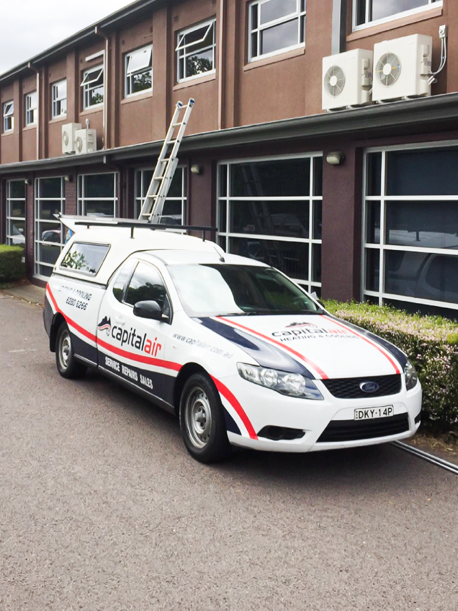 Capital Air service van parked outside a commercial building with air conditioning units installed above.