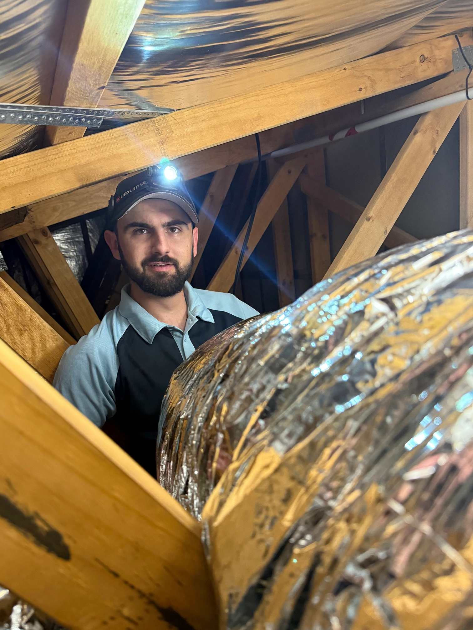  Air conditioning technician inspecting ducted system in roof space.