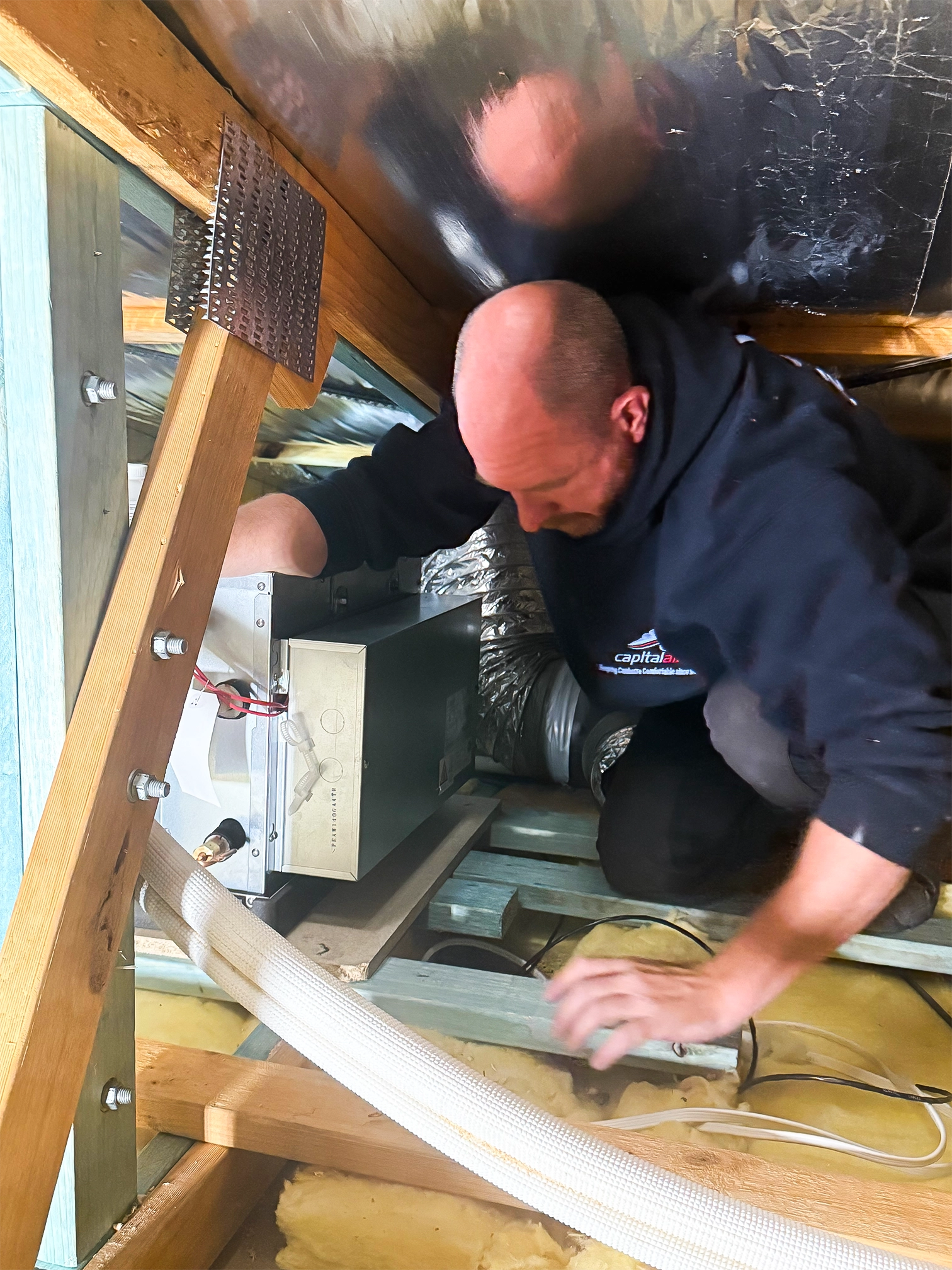 Capital Air technician servicing ducted heating and cooling equipment in a roof space.
