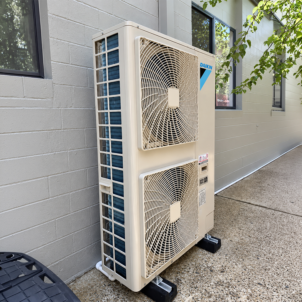 Daikin outdoor air conditioning unit with dual fans installed beside a building.