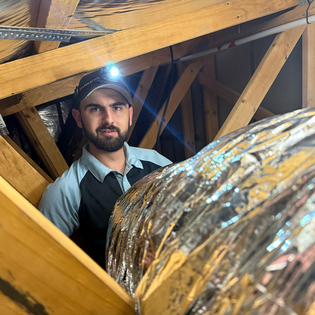 Capital Air technician working with insulated ductwork in a roof space.
