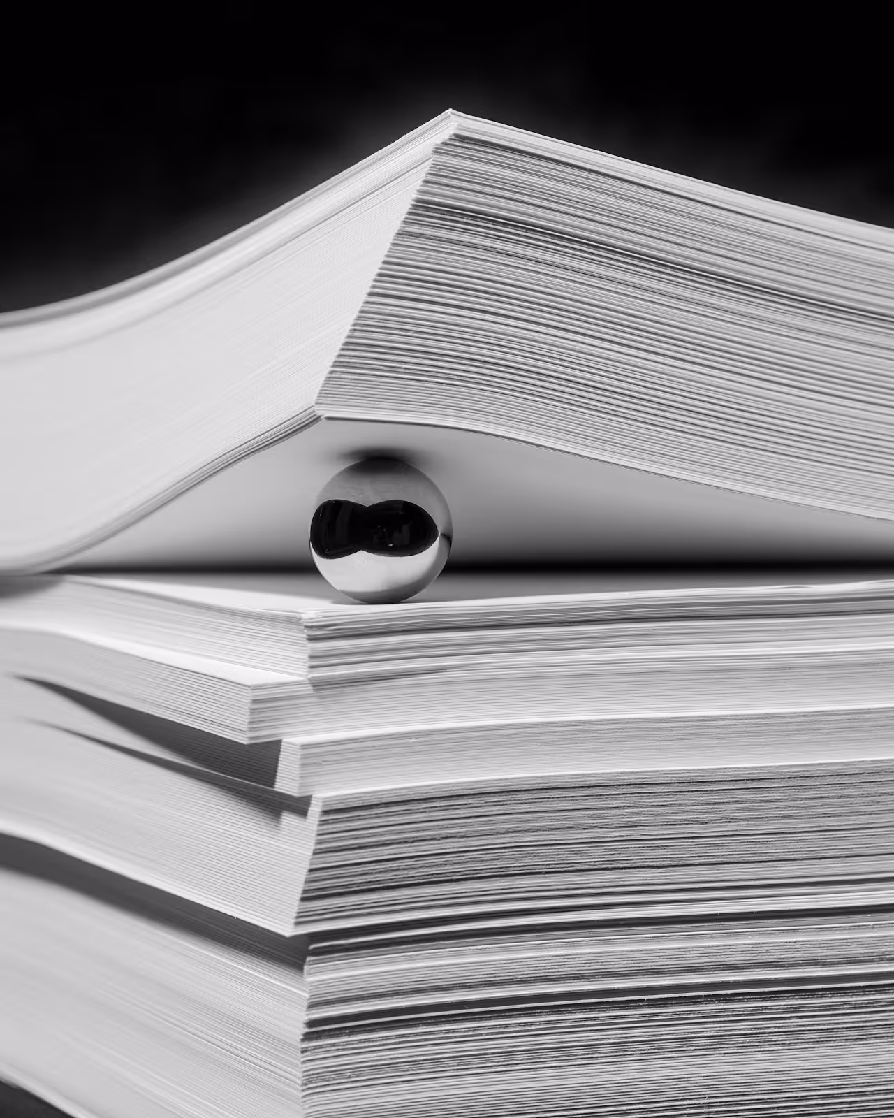 Schwarz-weiß-Bild von mehreren großen Buchstapeln mit einer Metallkugel, die einen Buchstapel auf dem anderen hält.