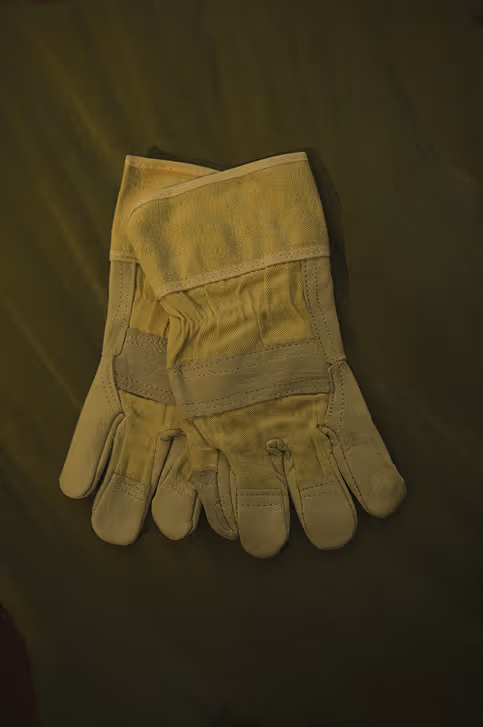 Paar arbeitsgelbe Handschuhe aus Leder auf dunkelgrünem Hintergrund.