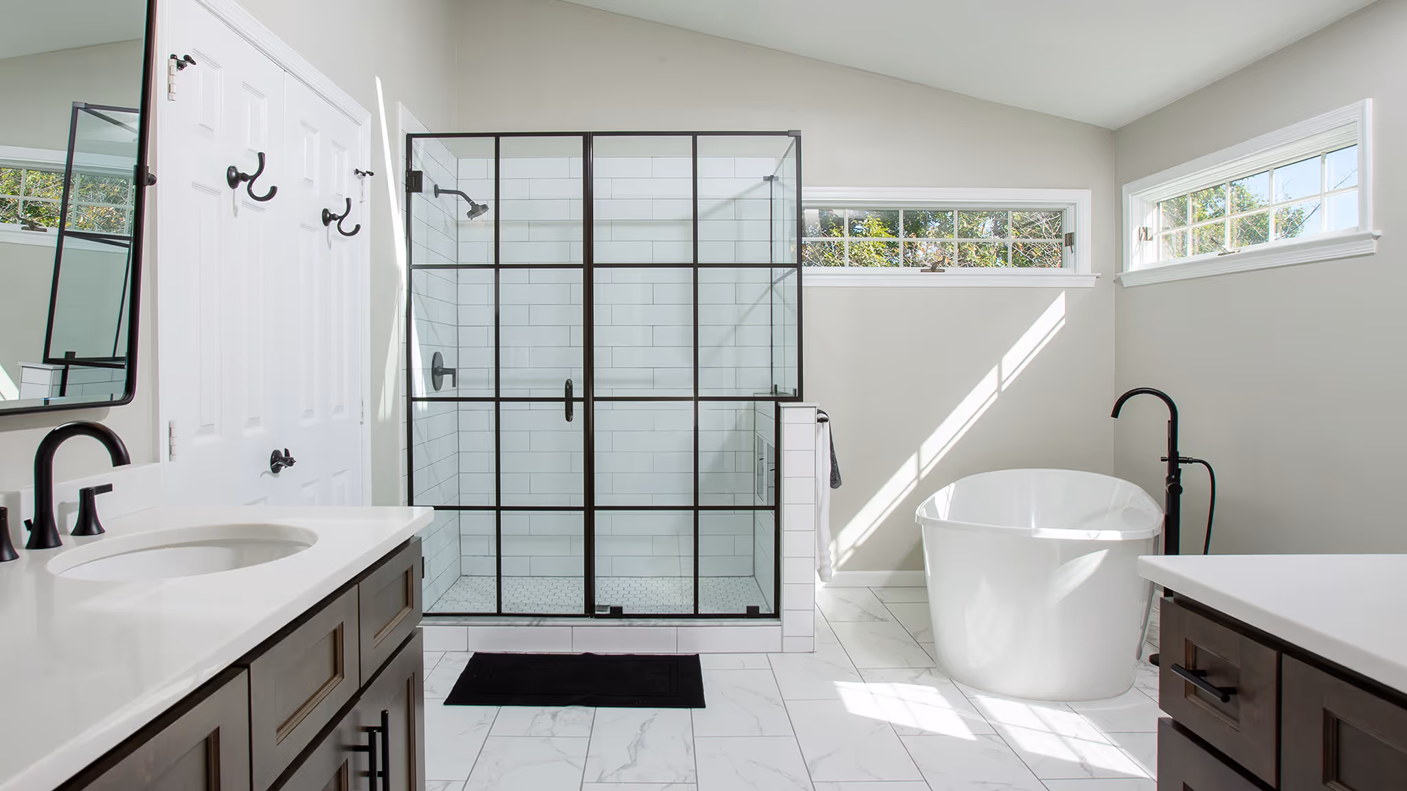 Modern bathroom with a glass shower enclosure, freestanding white bathtub, and double sink vanity with dark wood cabinets.