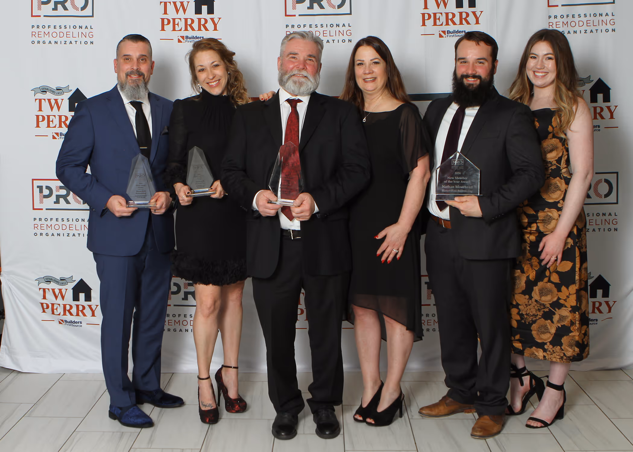 Six people dressed formally, standing in front of a Professional Remodeling Organization and TW Perry branded backdrop, three holding clear awards.