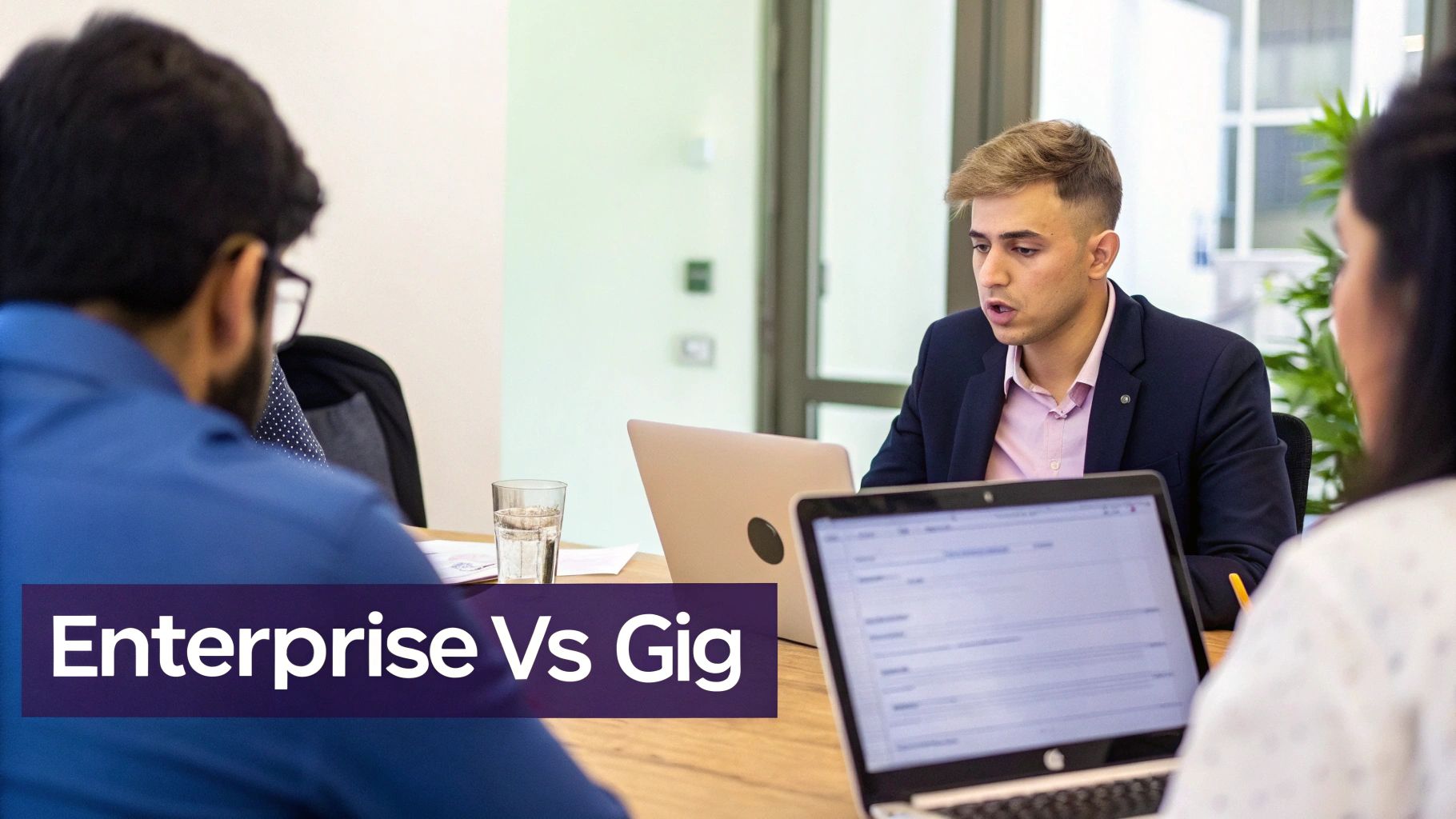 Three professionals in an office meeting with laptops, discussing 'Enterprise Vs Gig' work models.