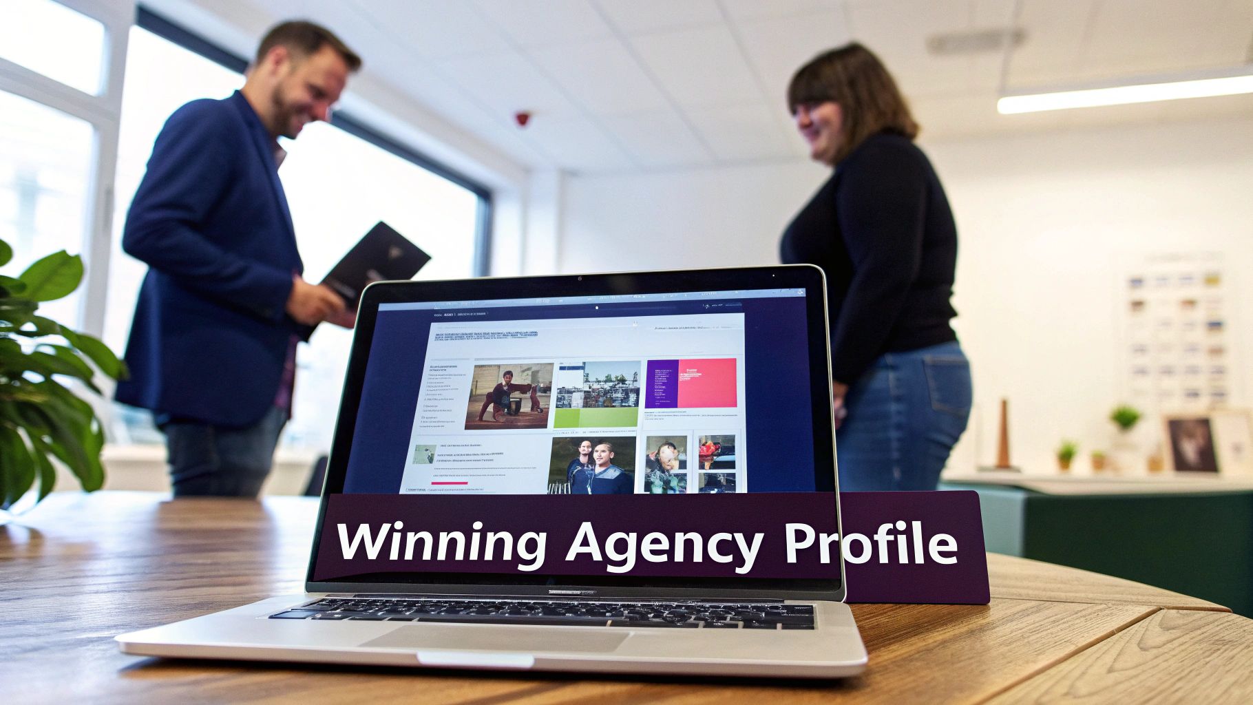 Laptop on a wooden desk displaying an agency profile, with two blurred people in a modern office.