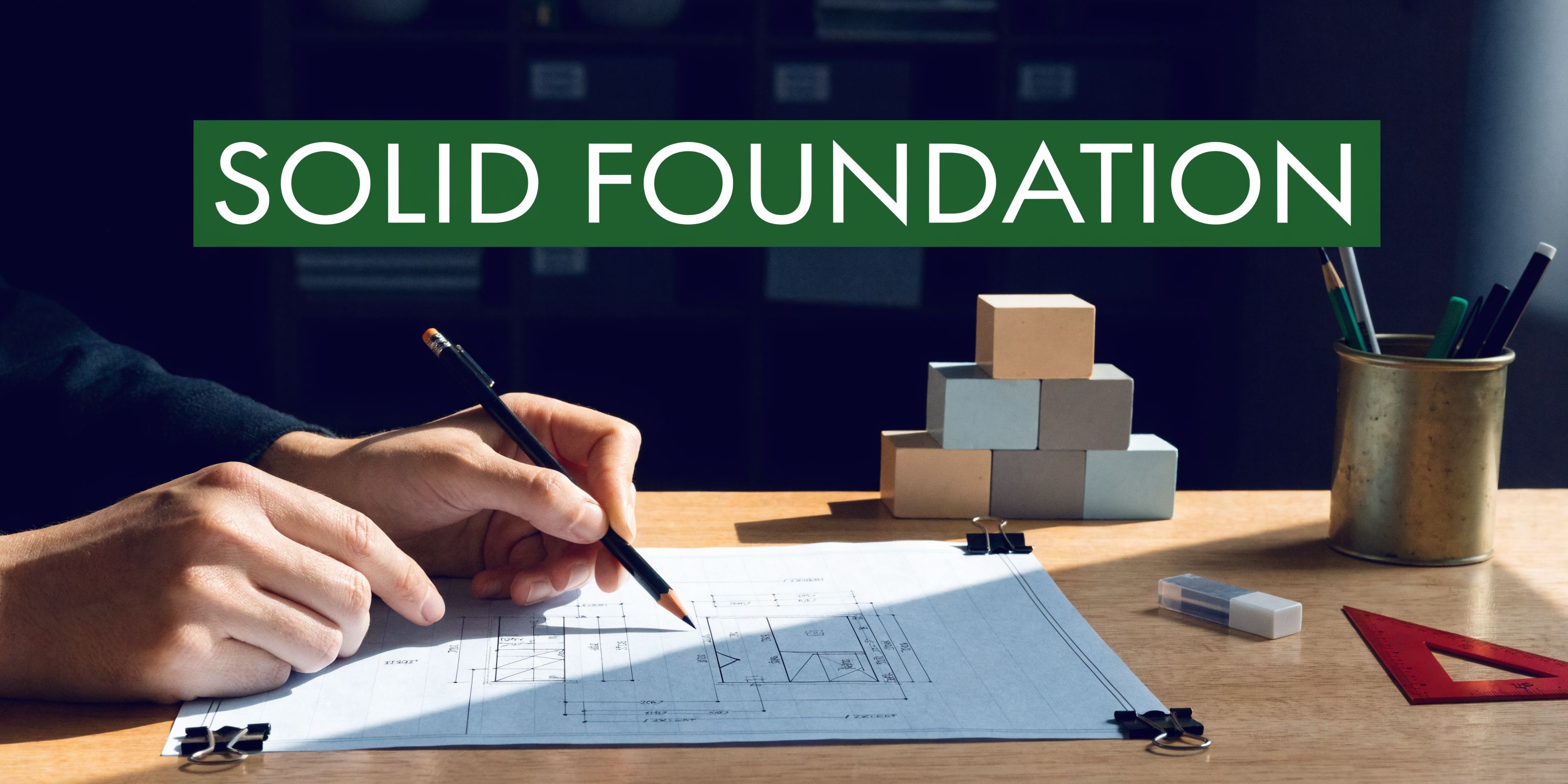 A professional architect sketching architectural plans on a desk with building blocks and drafting tools nearby.