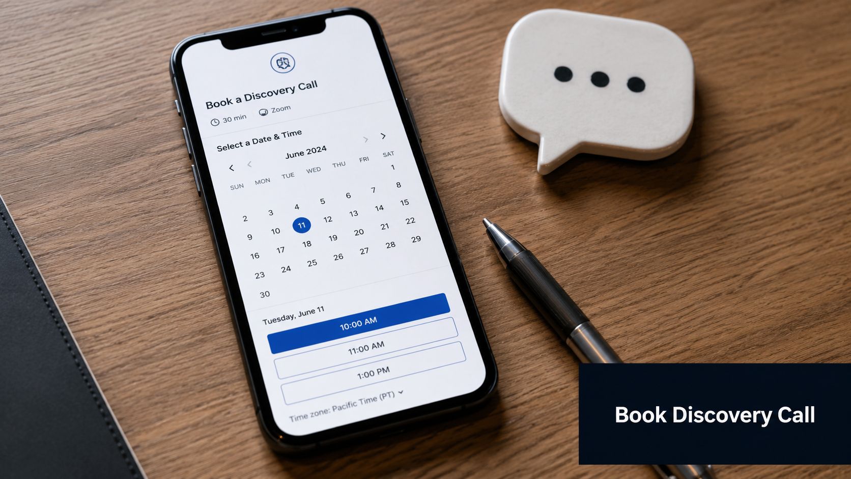 A smartphone screen displaying a calendar for booking a discovery call on a wooden desk with a pen.
