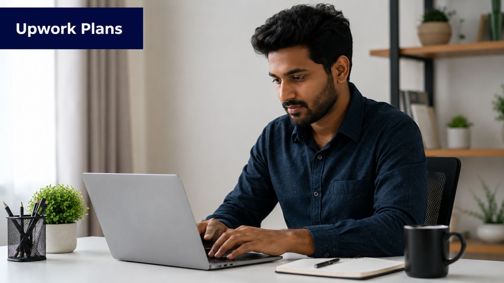 A professional man with a beard working on his silver laptop at a clean office desk