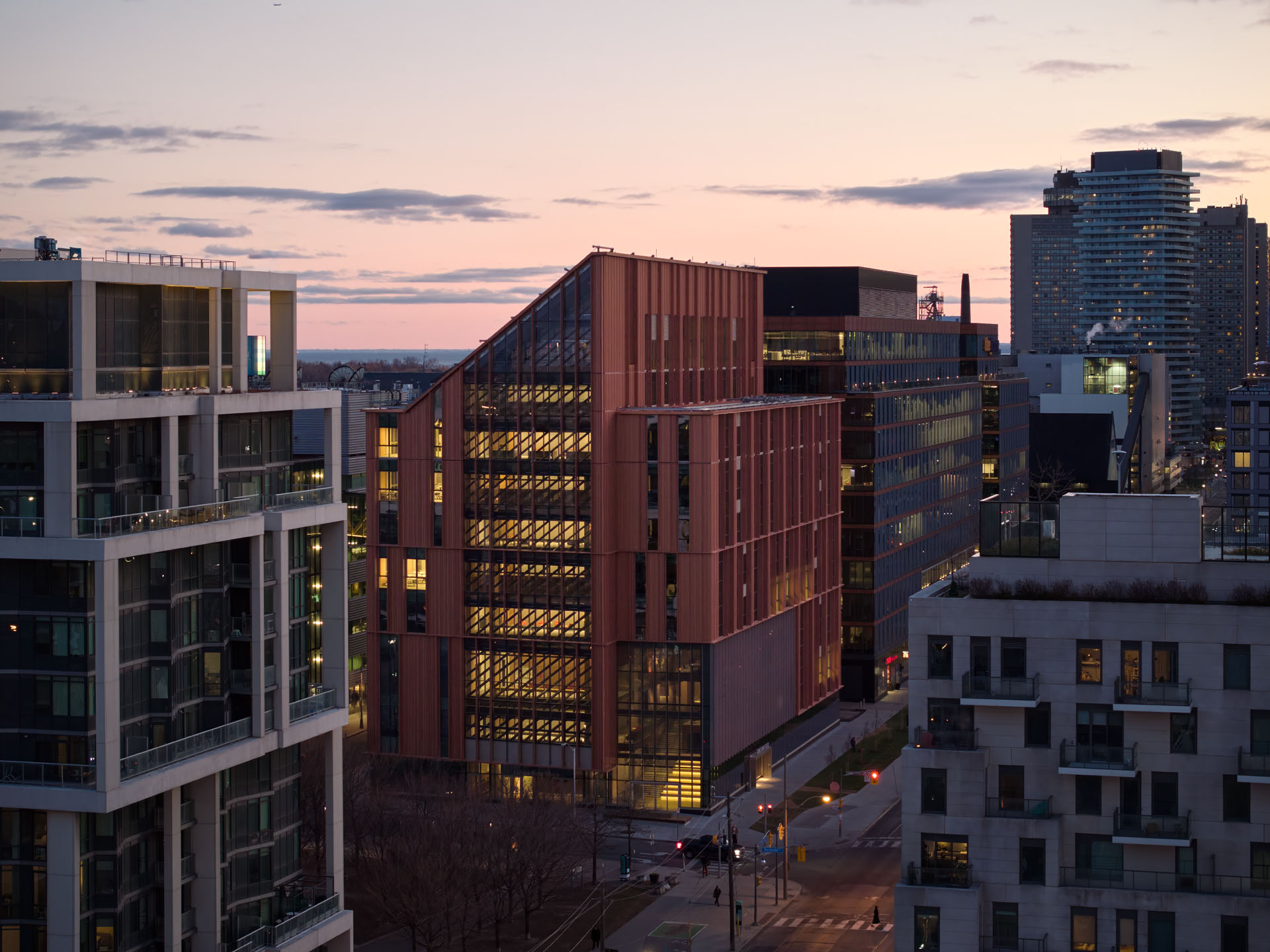 Evening cityscape featuring modern office buildings with illuminated windows under a colorful sunset sky.