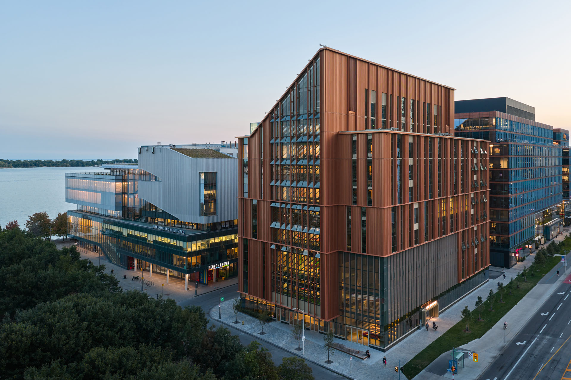 Modern buildings including George Brown College with red and glass facades near a waterfront at dusk.