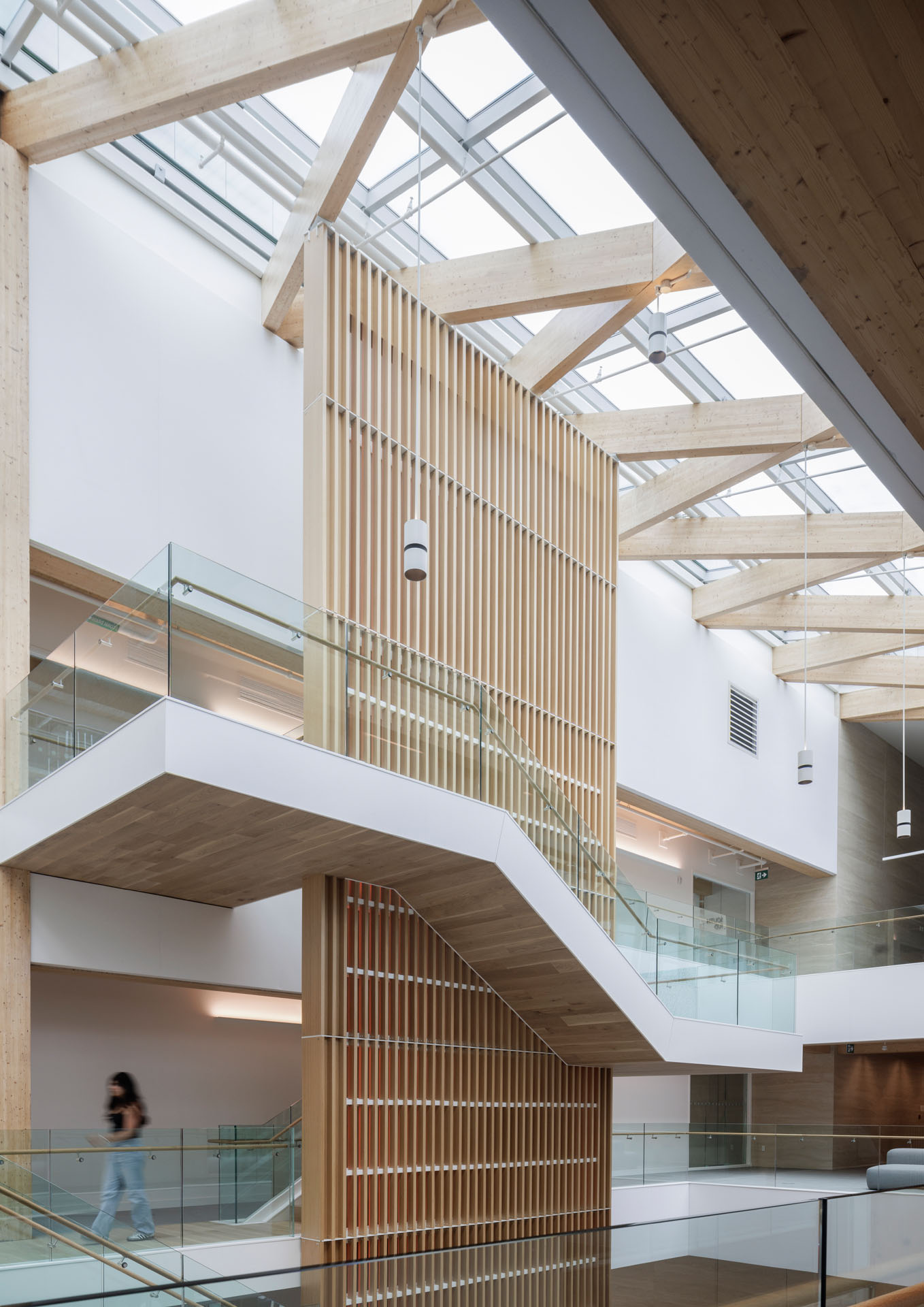 Modern interior with wooden beams, glass railings, vertical wooden slats, and a staircase under a glass ceiling.