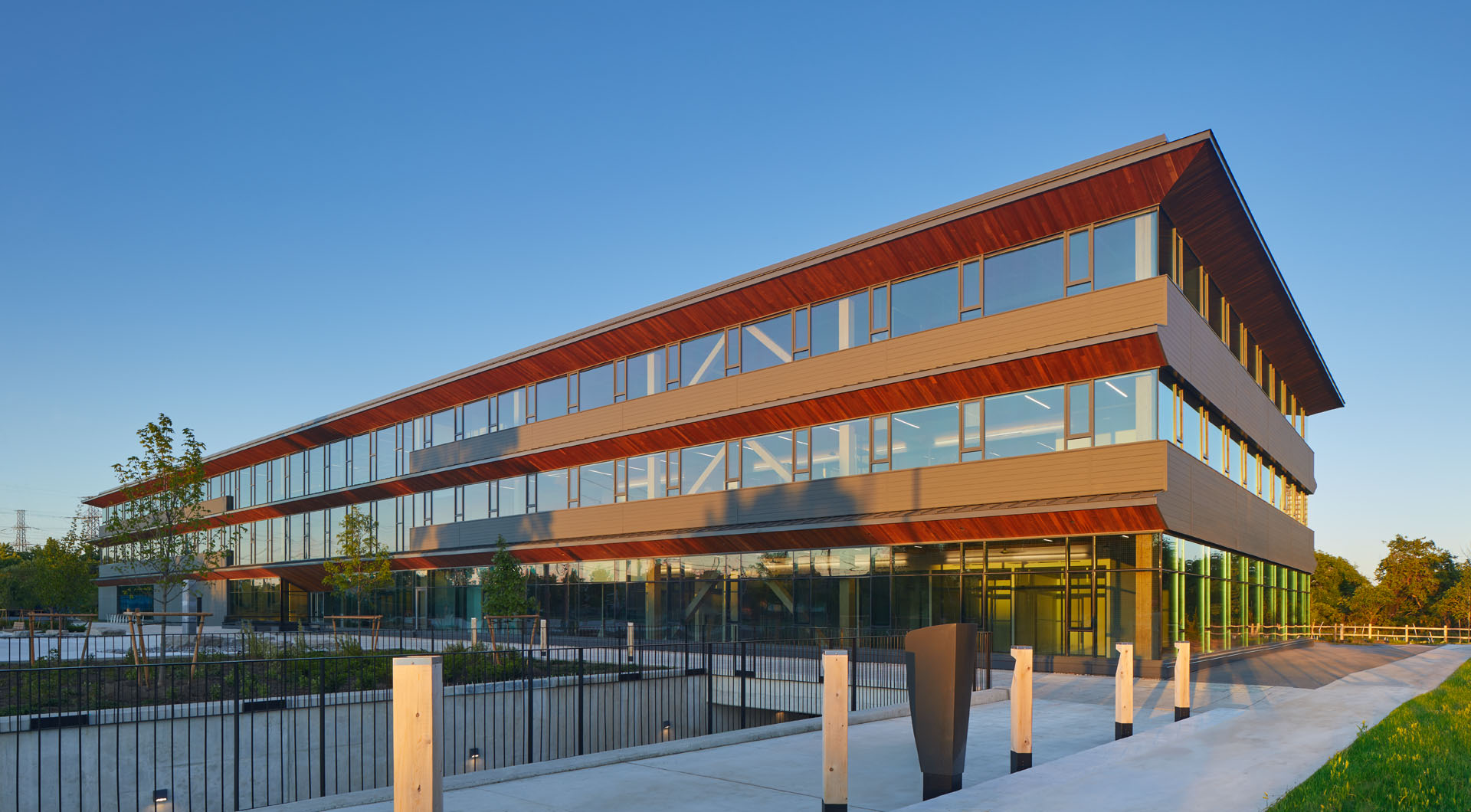 Modern three-story office building with large glass windows and wooden accents under a clear blue sky.
