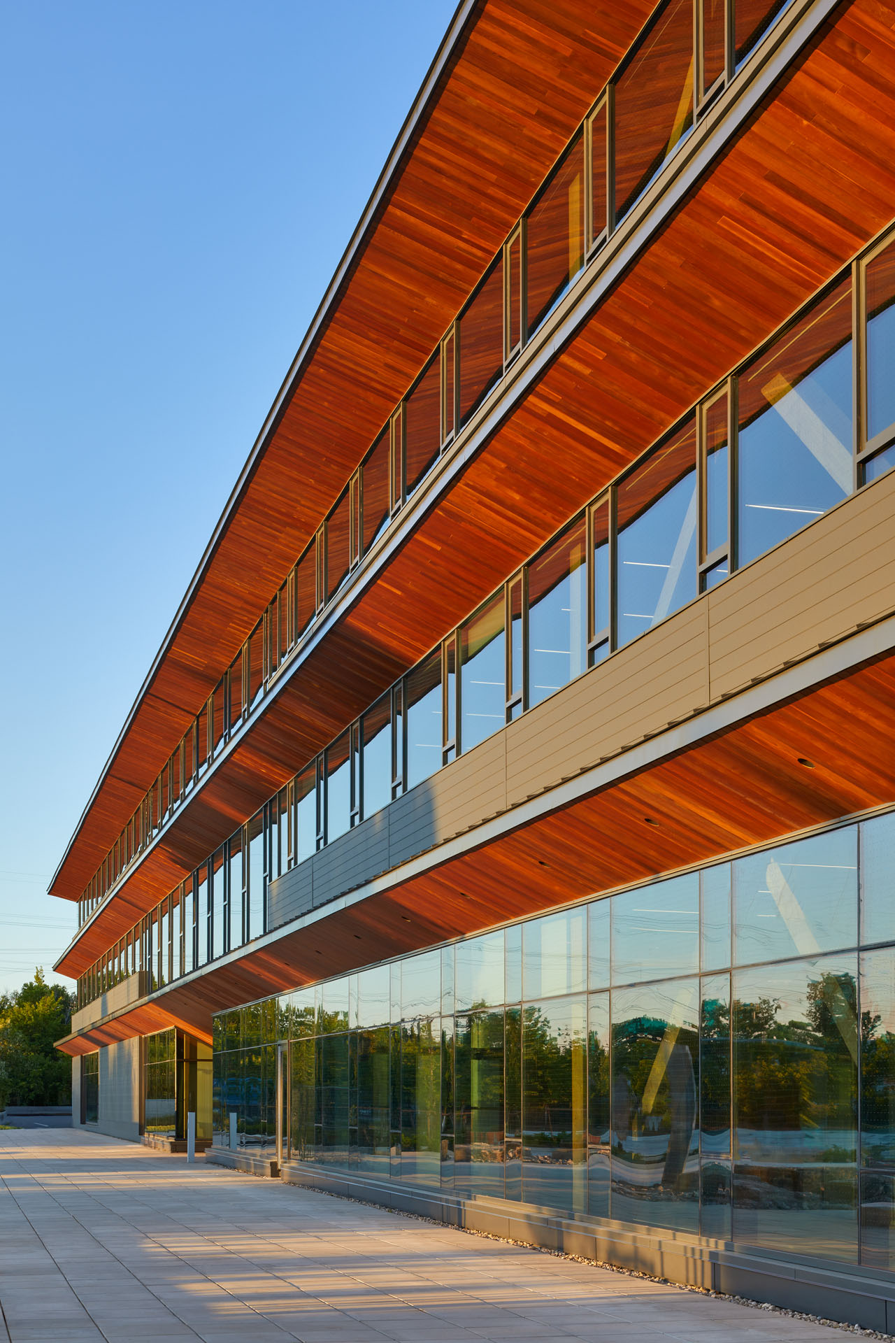 Modern building with large glass windows and warm wooden paneling under a clear blue sky at sunset.