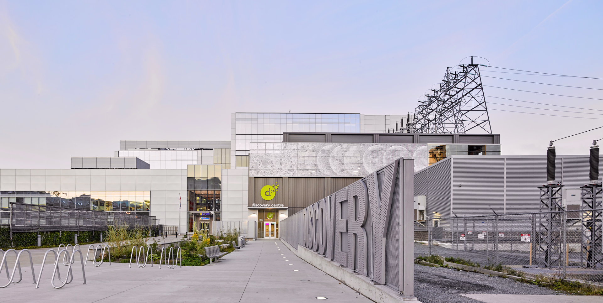 Exterior view of the Discovery Centre building with large metal letters spelling ‘DISCOVERY’ on a fence and a clear sky background.