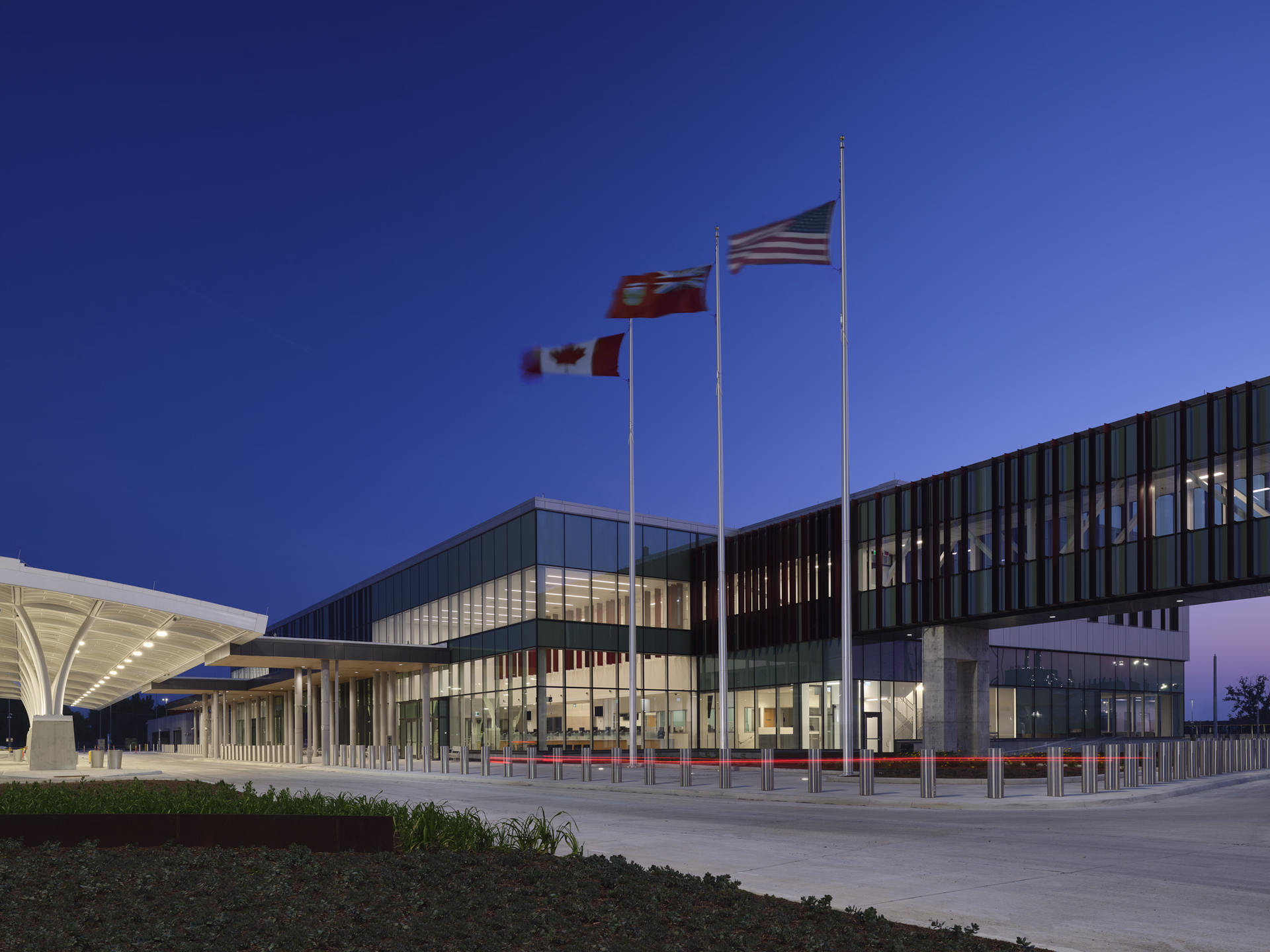 Modern glass building at dusk with American, Canadian, and Bermudian flags flying on flagpoles.
