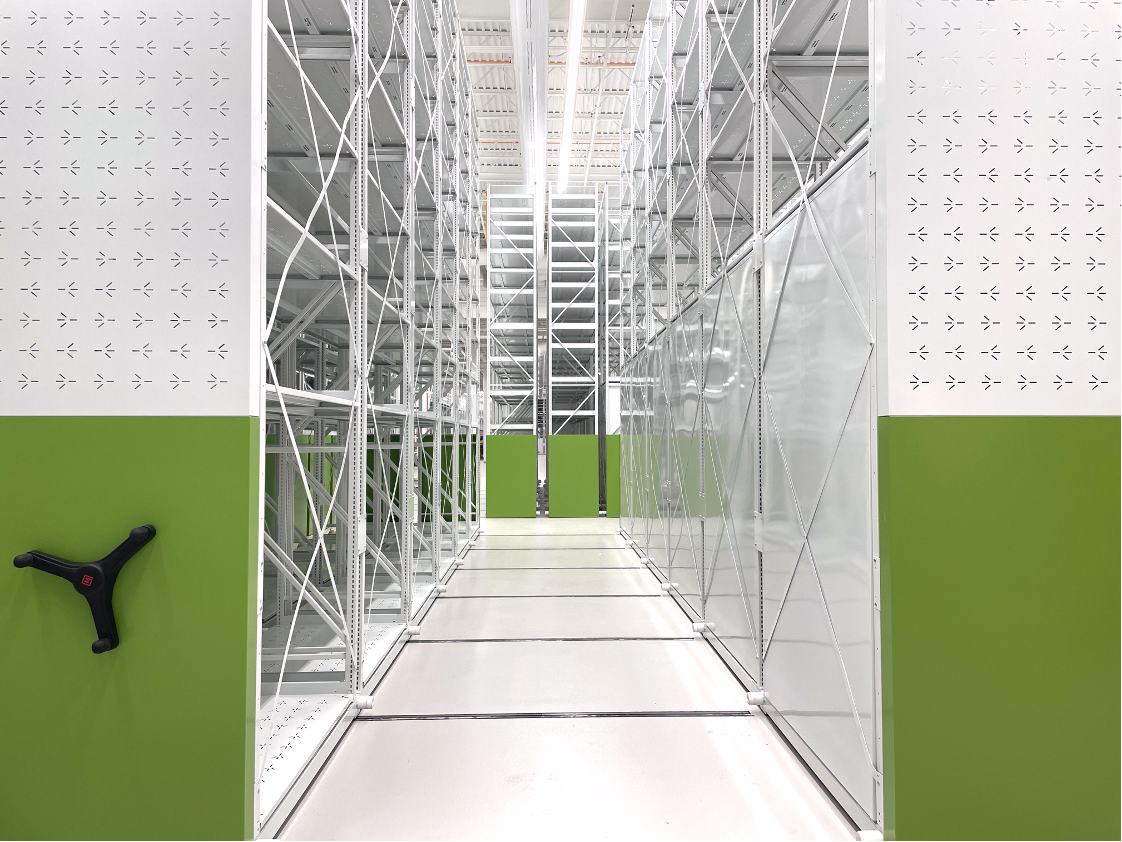 Empty industrial storage room with tall white and green metal shelving units on either side and a clean white floor.