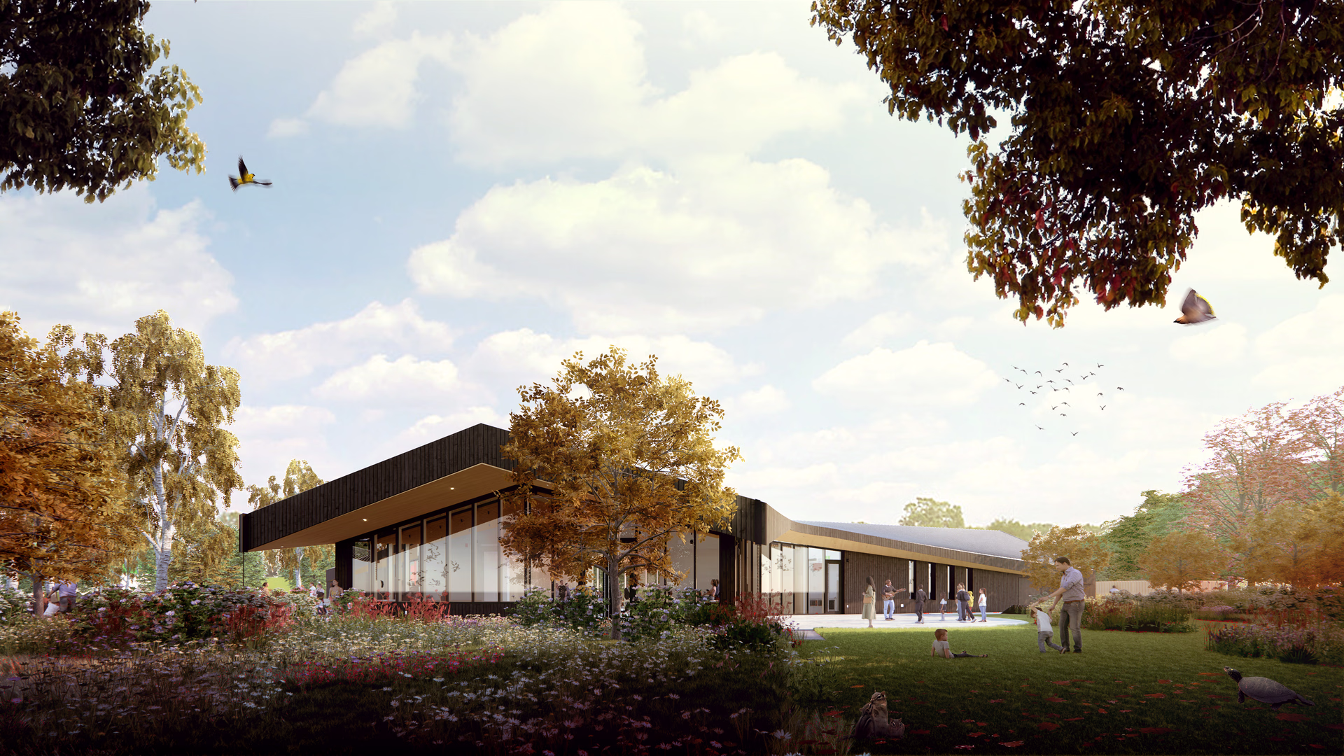 Modern single-story building with large windows surrounded by autumn trees, flowers, and people enjoying outdoor activities.