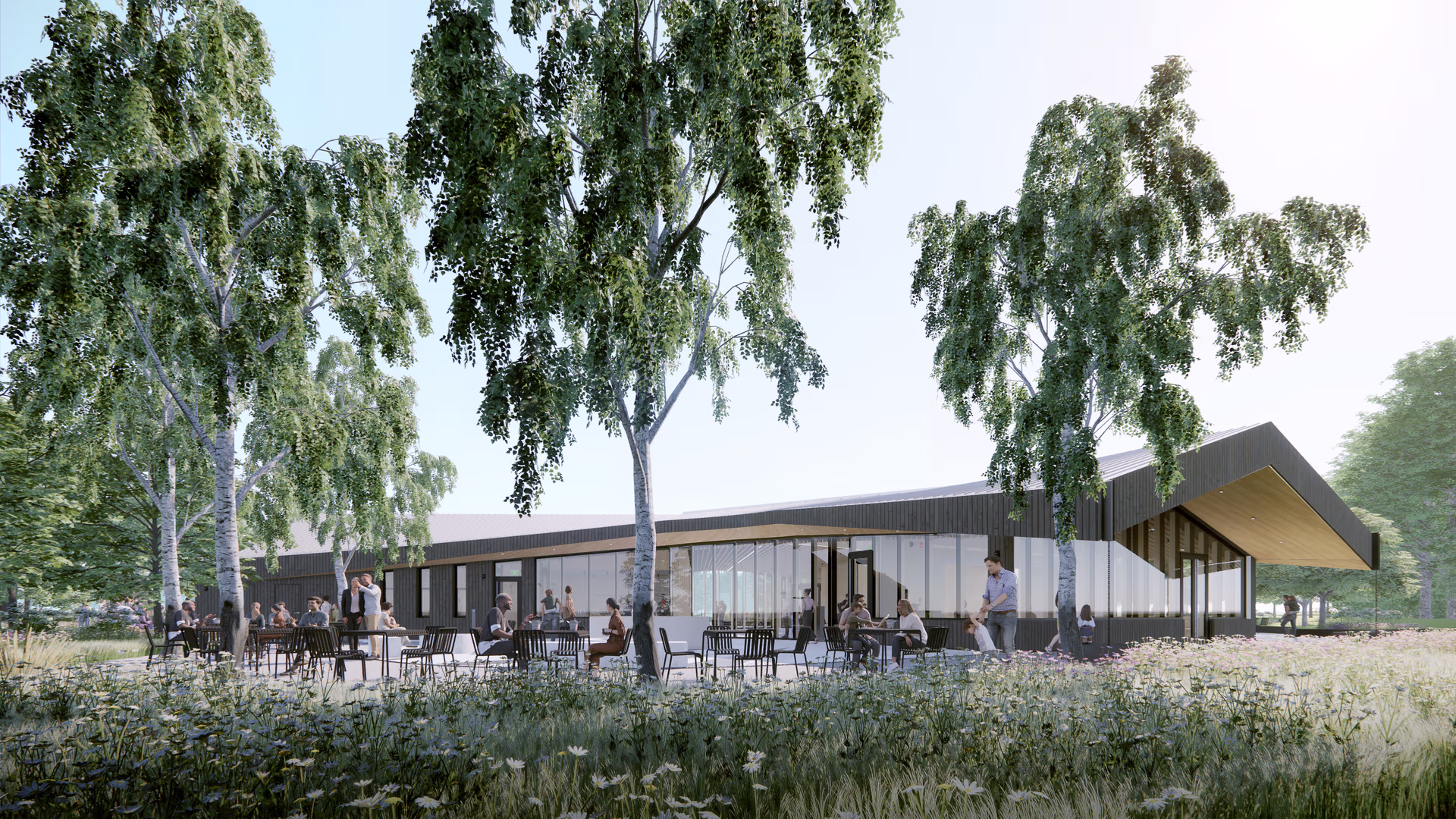 Modern single-story building with outdoor seating surrounded by trees and wildflowers, with people dining and socializing.