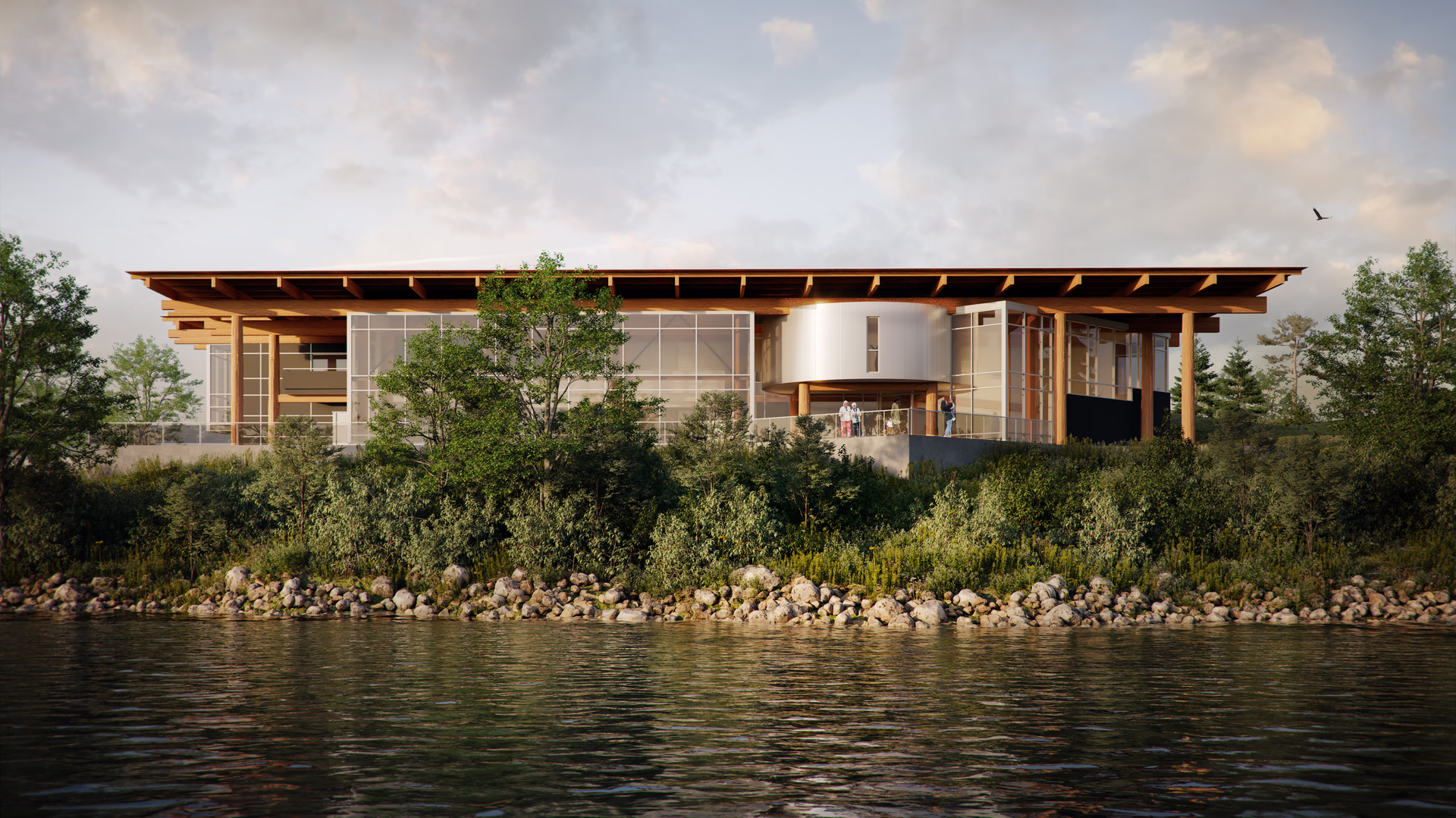 Modern glass and wood building on a hillside overlooking a river with trees and bushes in front.
