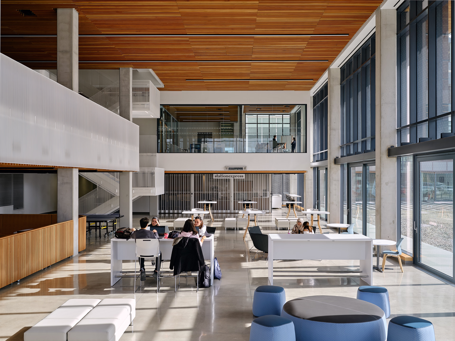 Modern open indoor workspace with people seated at desks and large floor-to-ceiling windows on the right.