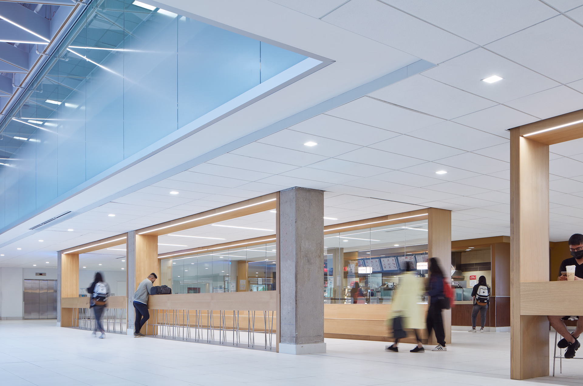 Modern indoor café area with wooden counters, stools, and blurred people walking and sitting.