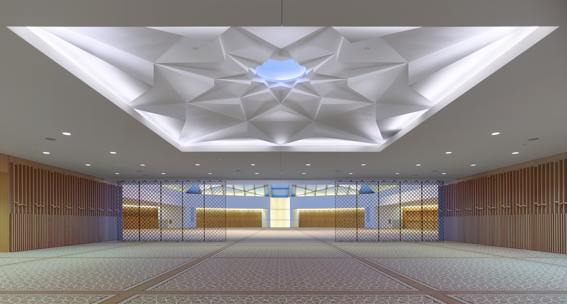 Spacious modern interior with geometric ceiling design featuring a blue skylight, patterned floor tiles, and wood-paneled walls.