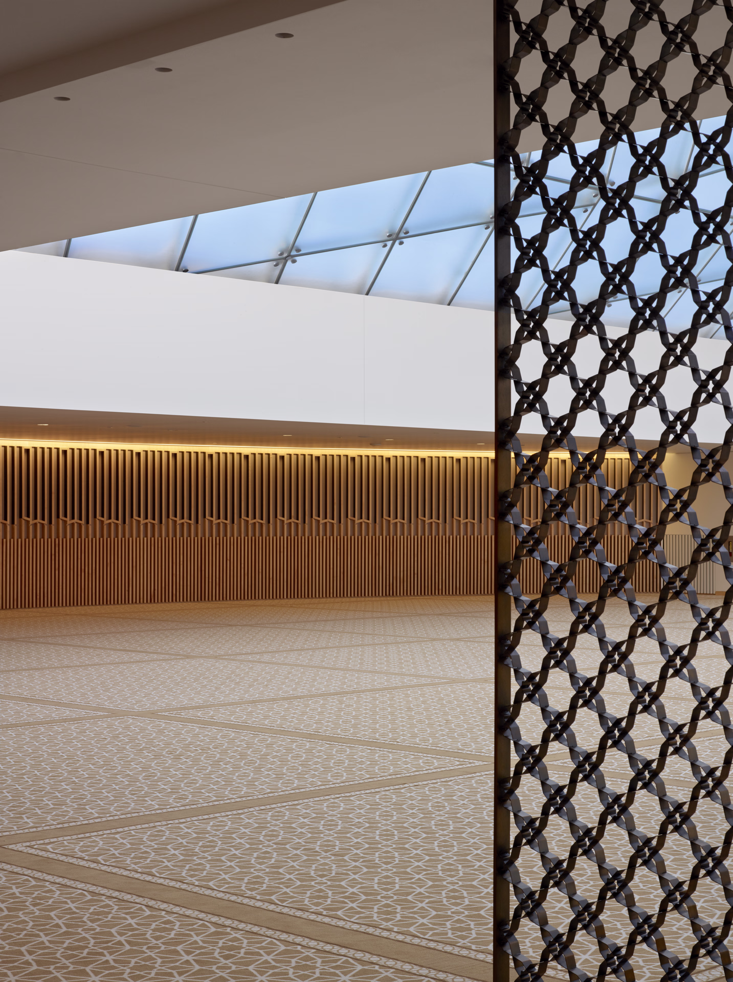 Spacious room with patterned carpet, wooden slat wall paneling, skylight ceiling, and a decorative black lattice panel on the right.