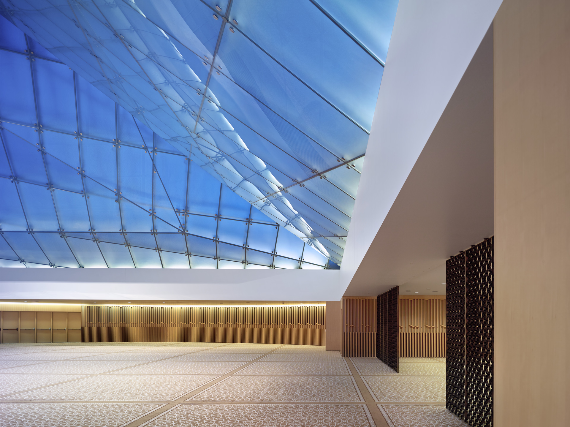 Spacious modern room with patterned floor, wood-paneled walls, and large blue-tinted glass ceiling.