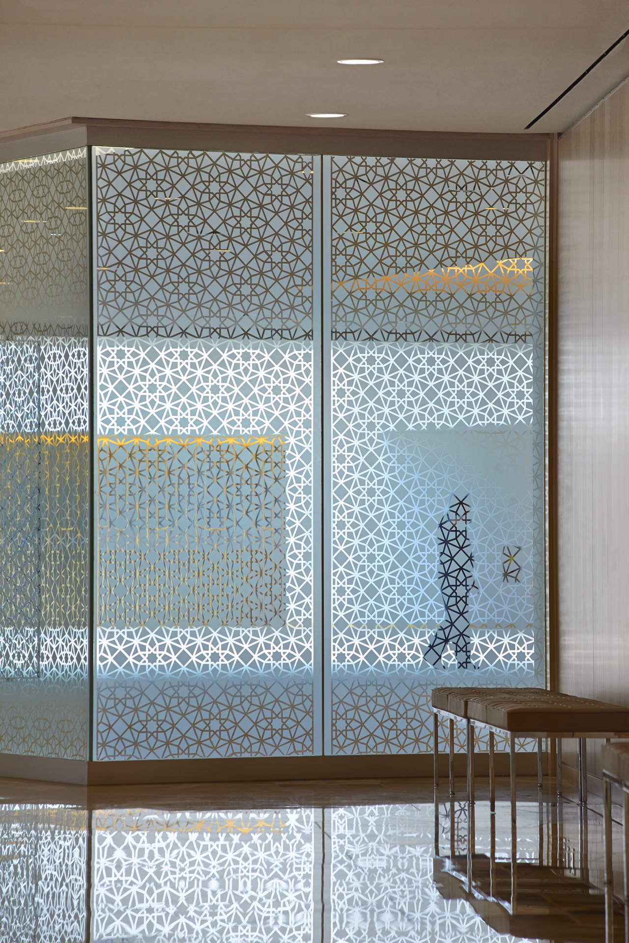 Silhouette of a person walking behind glass panels with intricate geometric patterns in a modern interior space.