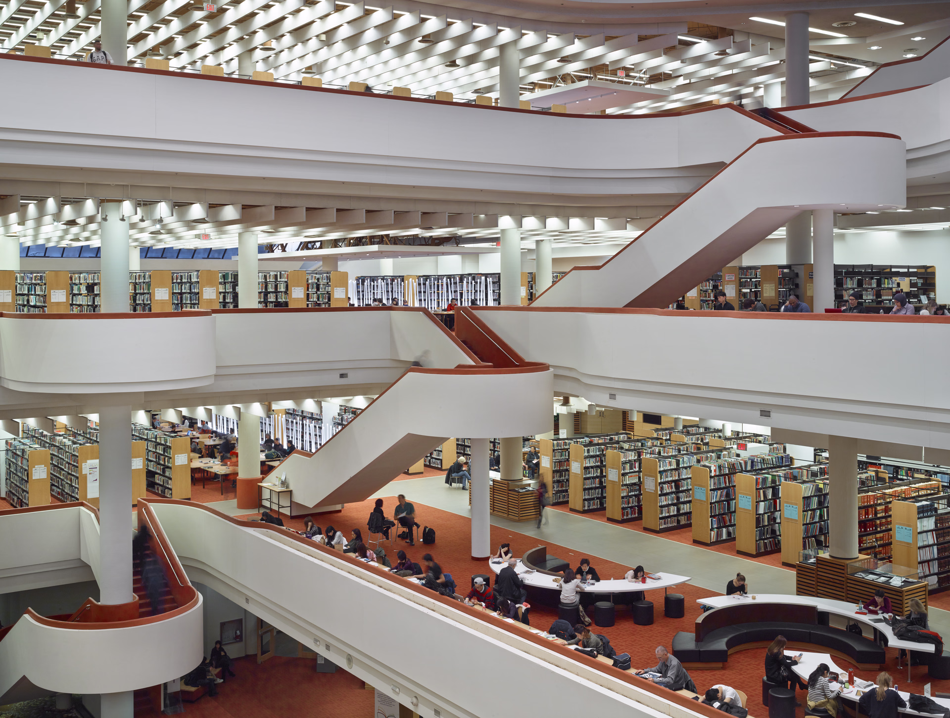 Multi-level modern library interior with rows of bookshelves, study tables, and people reading and working.
