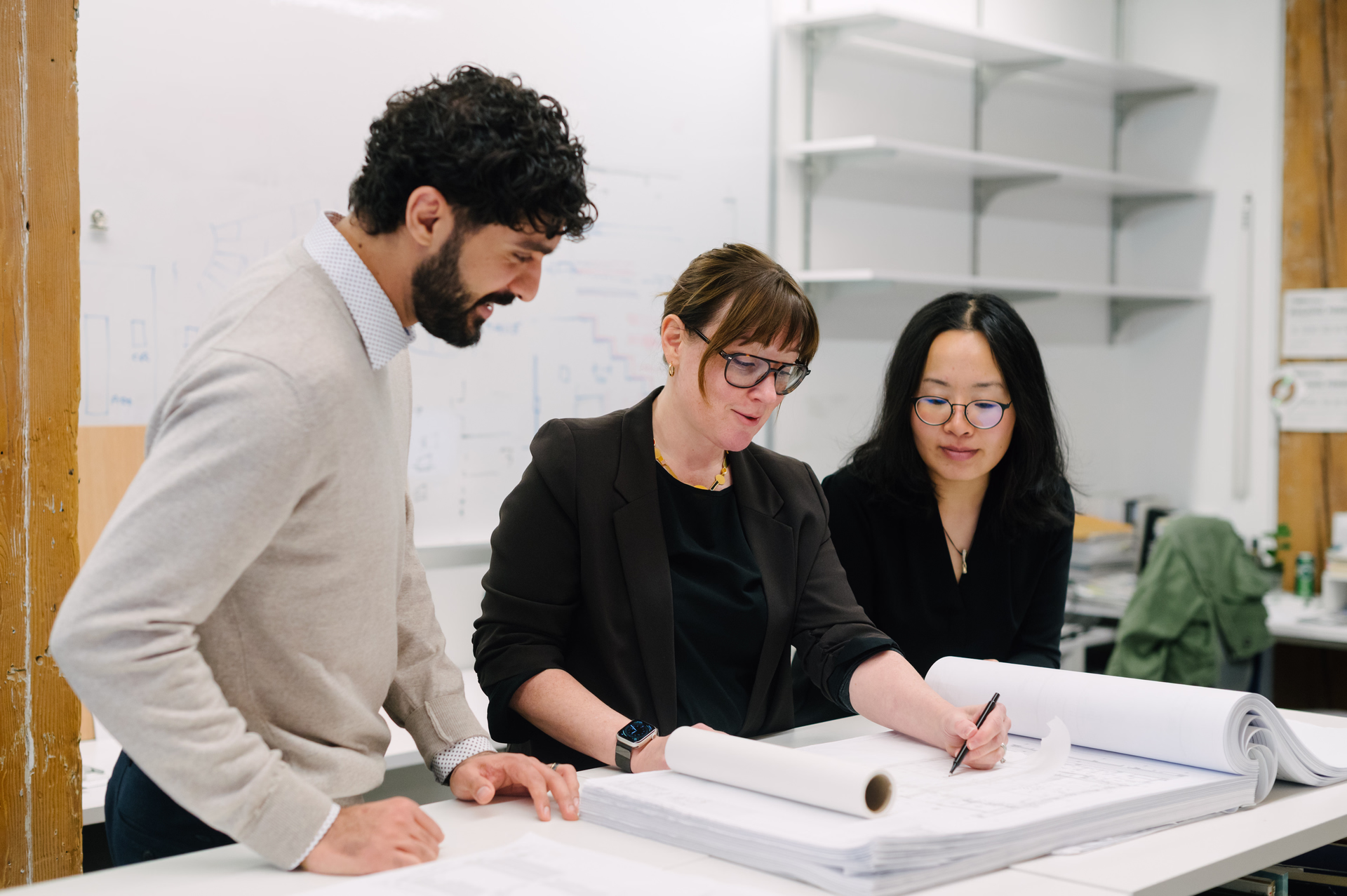 Three colleagues in an office reviewing architectural blueprints on a desk.